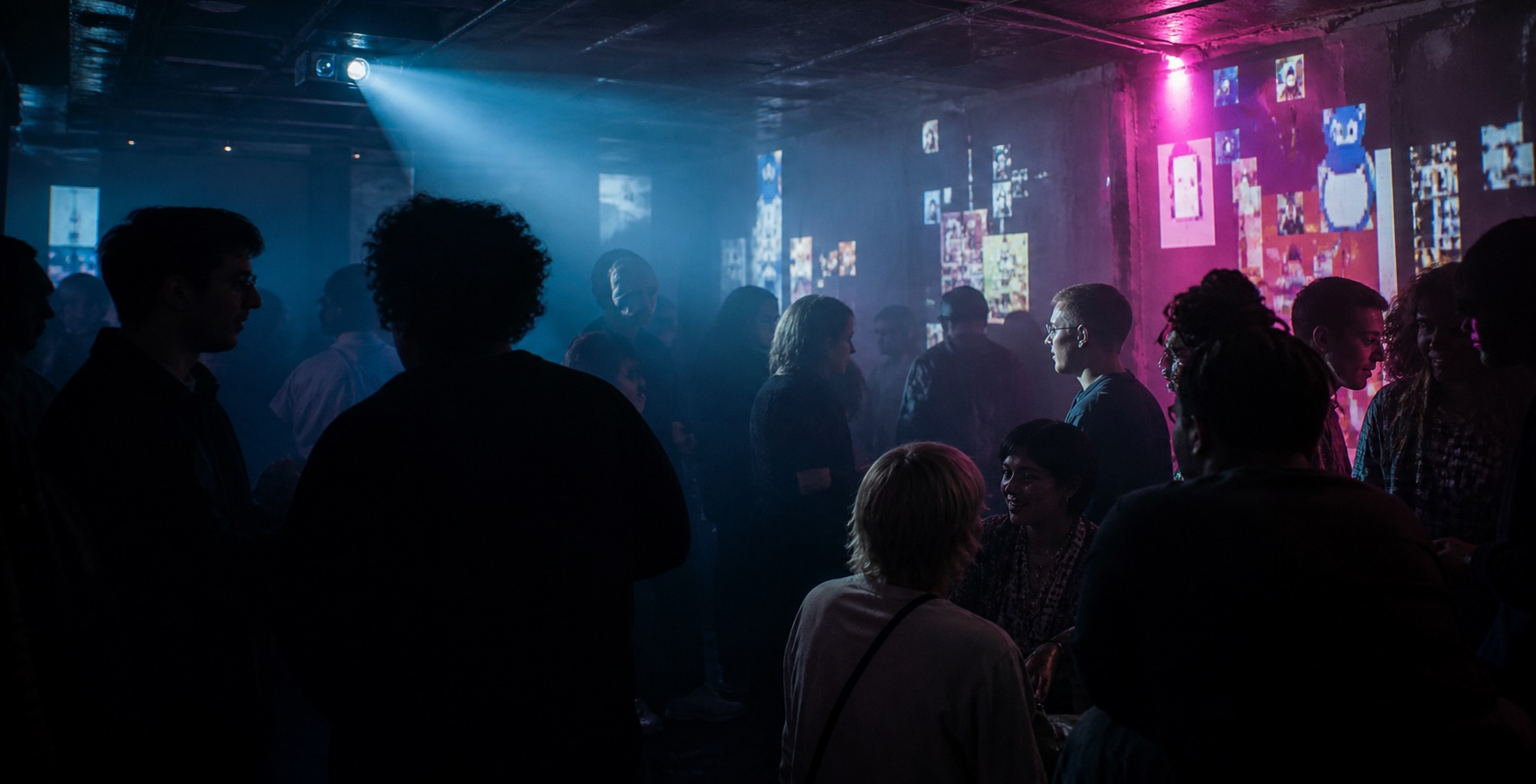 People gathered beneath blue and magenta projections at an underground Descarded event.